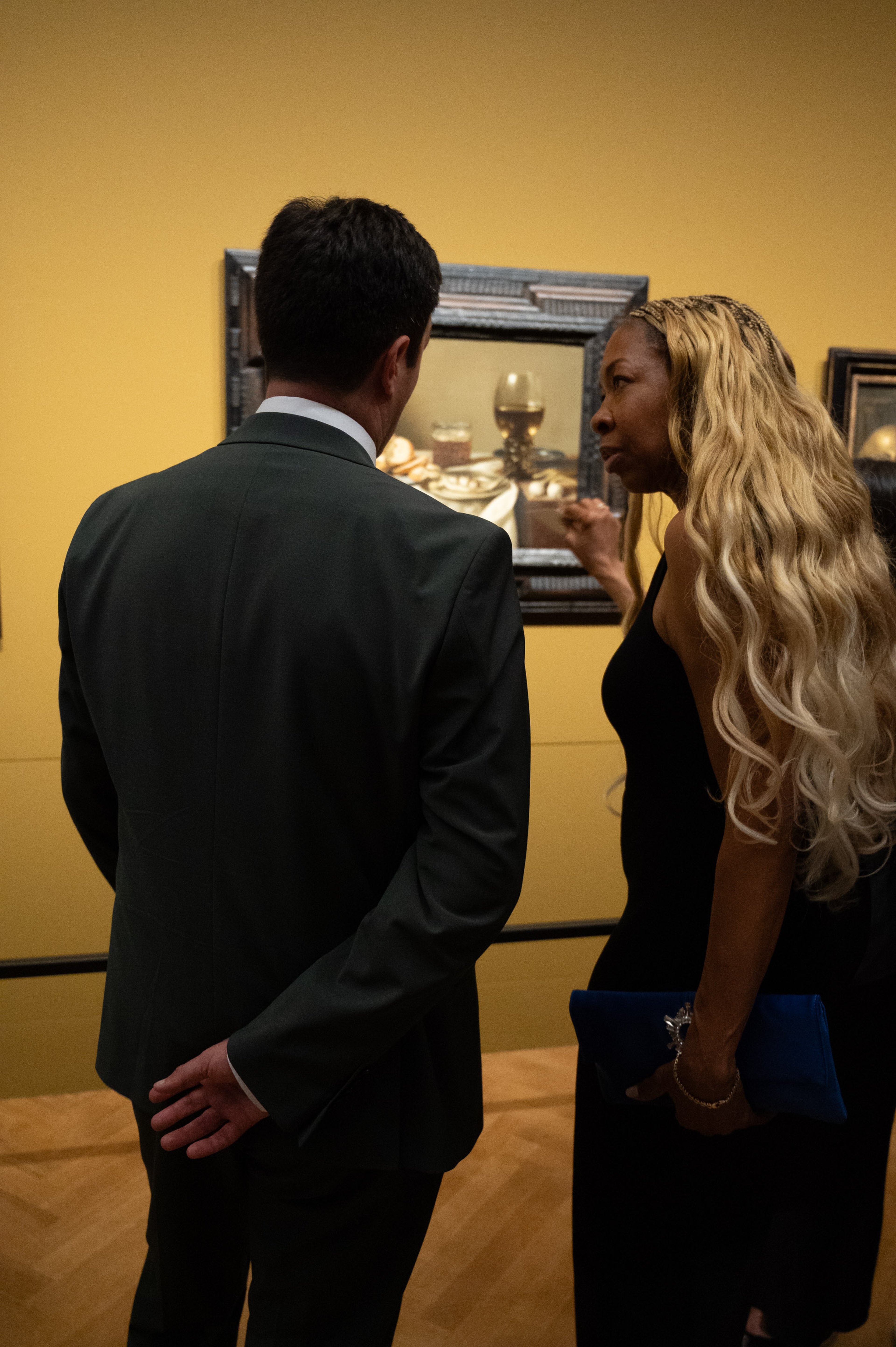 Hier sind ein Mann und eine Frau vor einem der Gemälde von Pieter Claesz im Kunsthistorischen Museum zu sehen. Die beiden sind von hinten zu sehen, wobei die Frau sich leicht zum Mann gedreht hat und offenbar gerade etwas sagt.